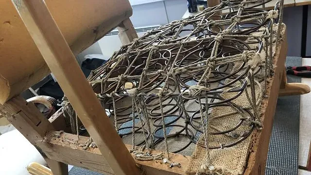 Omtrekking av stol med synlige fjærer, tau og treramme under setet